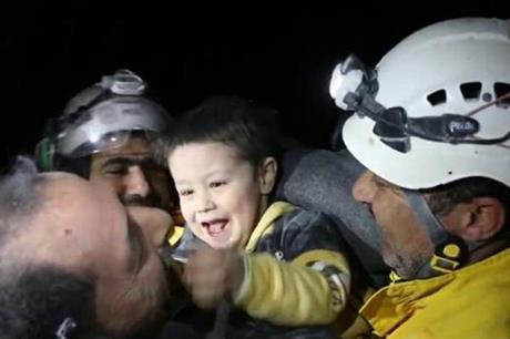 شاهد طفل سوري يخرج ضاحكاً من تحت الأنقاض ويداعب رجال الإنقاذ